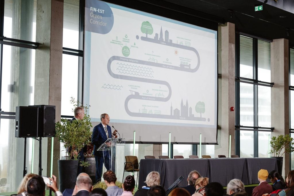 Two men present to a conference in front of a screen showing a graphic portraying the green journey available for users of the Tallinn to Helsinki green corridor