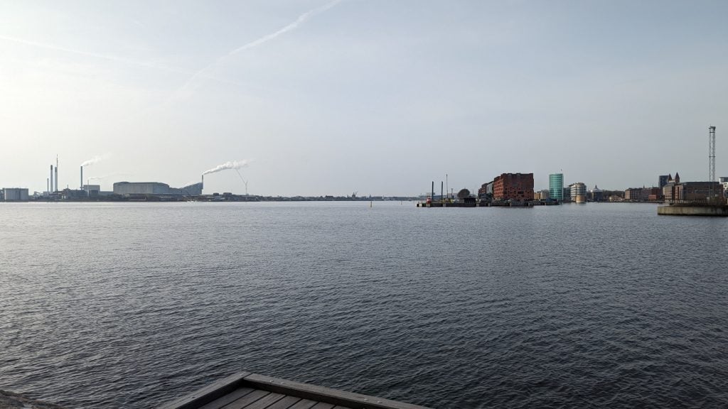A harbour in Copenhagen with buildings across the water and a factory billowing steam